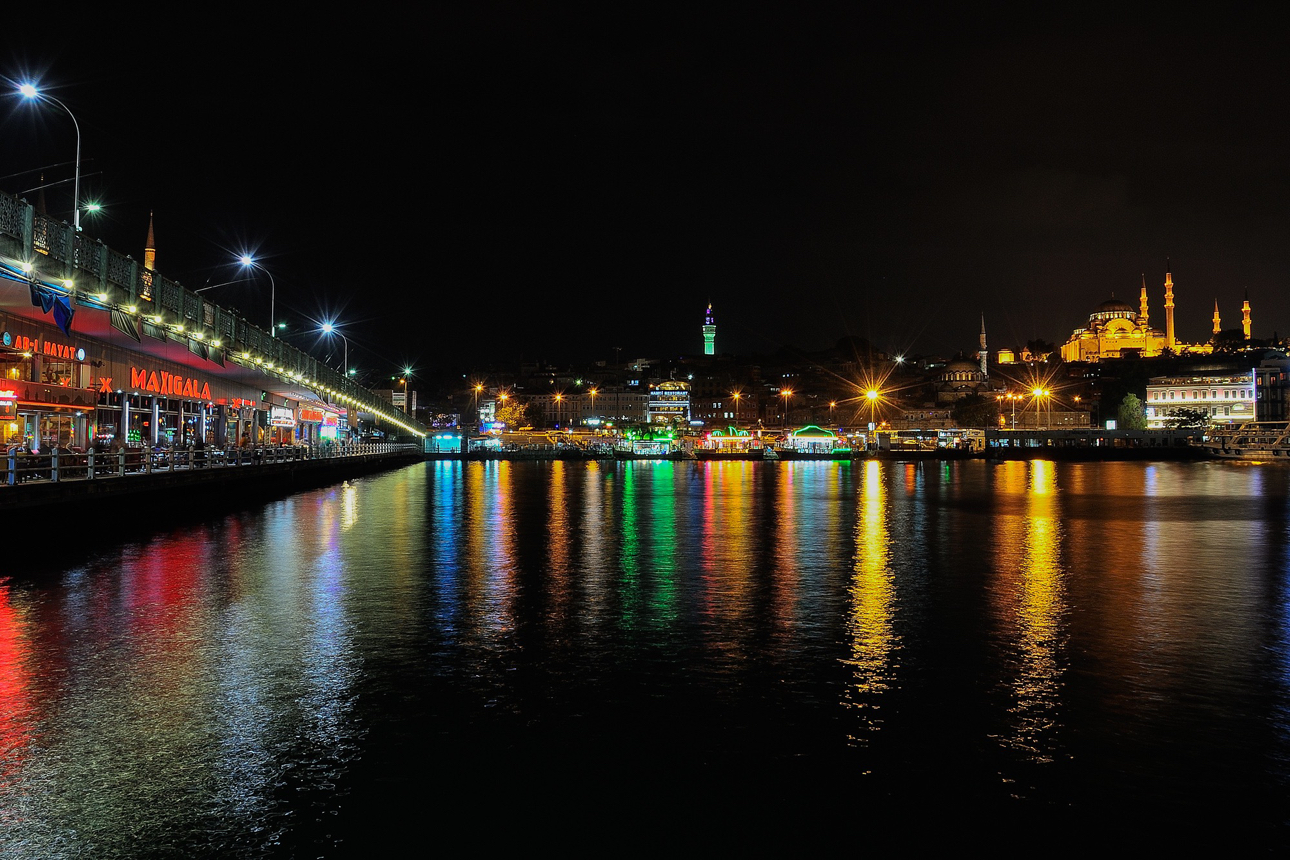 Skyline di Istanbul, si possono distinguere le sagome illuminate di edifici e moschee iconiche, come la Moschea di Solimano (S&uuml;leymaniye Camii), la foto &egrave; stata scatta dalla base di un pilone del Ponte di Galata